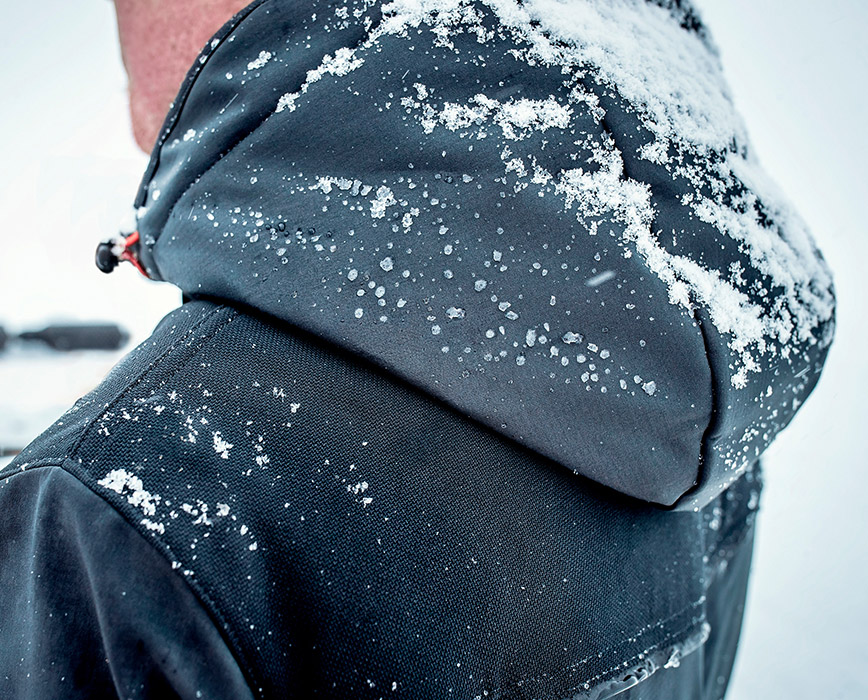 DRaußen im Schnee und bei kalten Temperaturen trägt MArtin die Winter Softshelljacke Stretch X in Blau mit praktischer und wasserdichter Kapuze